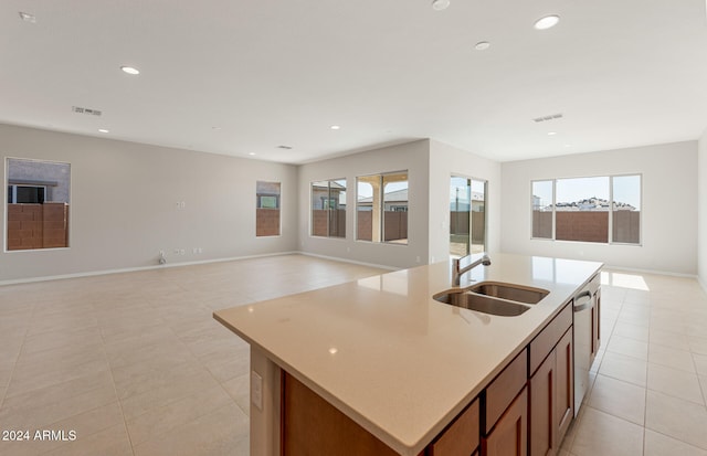 kitchen featuring dishwasher, sink, light tile patterned floors, and an island with sink