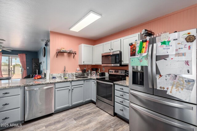 kitchen with light stone countertops, appliances with stainless steel finishes, ceiling fan, sink, and white cabinetry