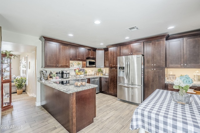 kitchen featuring visible vents, dark brown cabinets, wood tiled floor, light stone counters, and appliances with stainless steel finishes