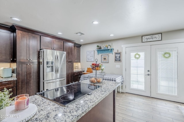 kitchen featuring visible vents, dark brown cabinets, stainless steel fridge with ice dispenser, cooktop, and light stone counters