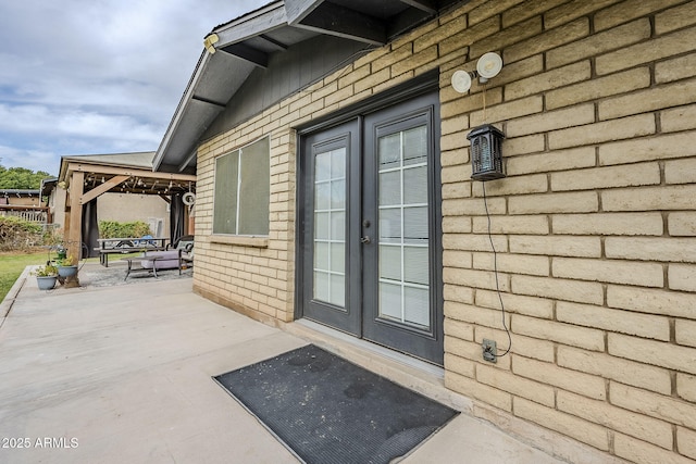 view of exterior entry with french doors, brick siding, and a patio area