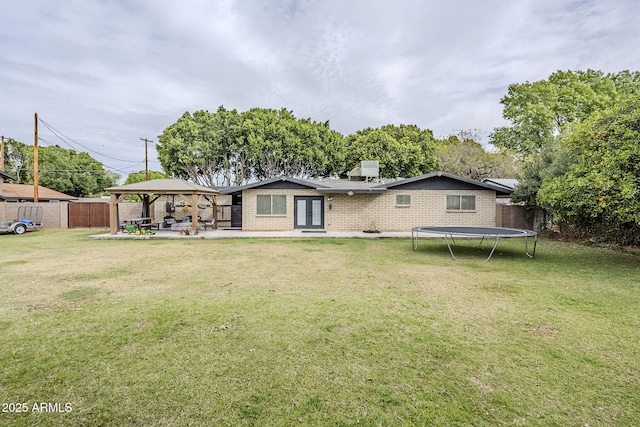 back of house with a gazebo, a trampoline, a lawn, and fence private yard