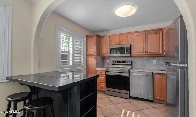 kitchen with a kitchen breakfast bar, decorative backsplash, light tile patterned floors, kitchen peninsula, and stainless steel appliances