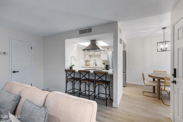 living area featuring visible vents, baseboards, light wood-style floors, and a chandelier