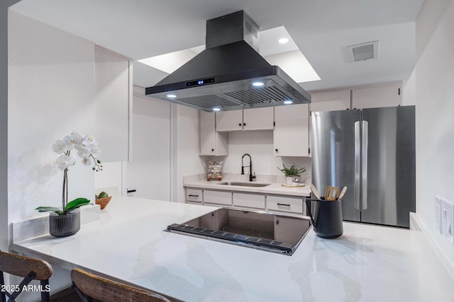 kitchen with visible vents, freestanding refrigerator, a sink, stovetop with downdraft, and island range hood