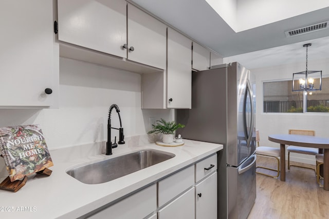 kitchen with visible vents, light countertops, freestanding refrigerator, white cabinets, and a sink