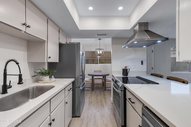 kitchen with visible vents, wall chimney range hood, appliances with stainless steel finishes, light wood-style floors, and a sink