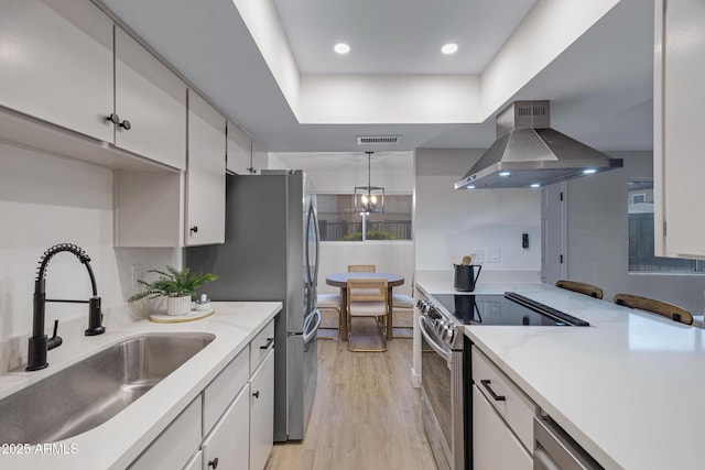 kitchen featuring visible vents, a sink, stainless steel appliances, wall chimney exhaust hood, and light wood-type flooring