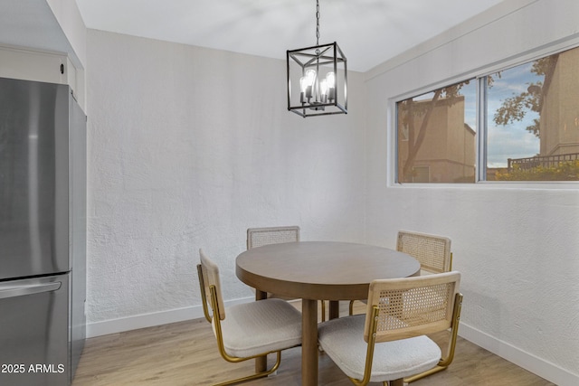 dining area featuring a textured wall, baseboards, a notable chandelier, and light wood finished floors