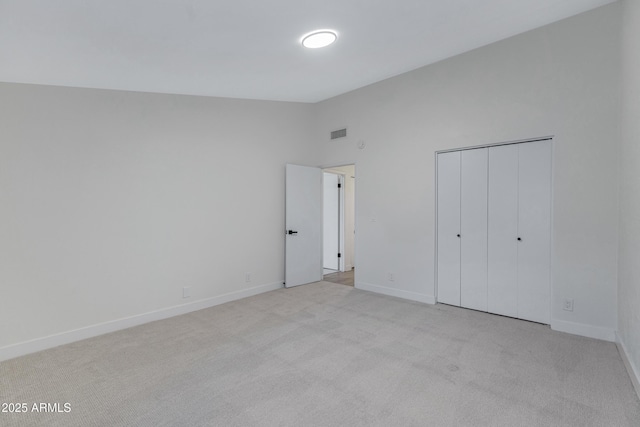 unfurnished bedroom featuring baseboards, visible vents, lofted ceiling, a closet, and carpet flooring