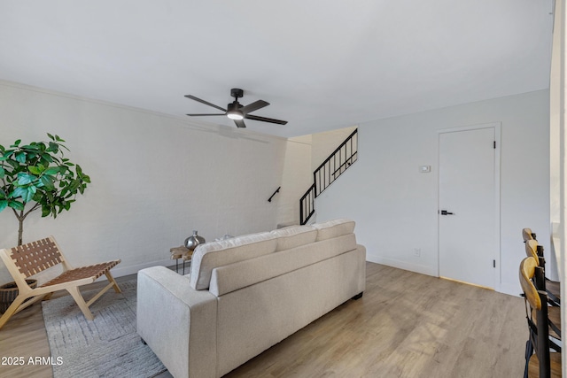 living room with baseboards, stairs, light wood-type flooring, and a ceiling fan