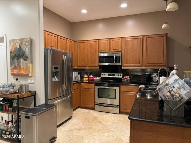 kitchen with appliances with stainless steel finishes, light tile floors, tasteful backsplash, dark stone countertops, and pendant lighting