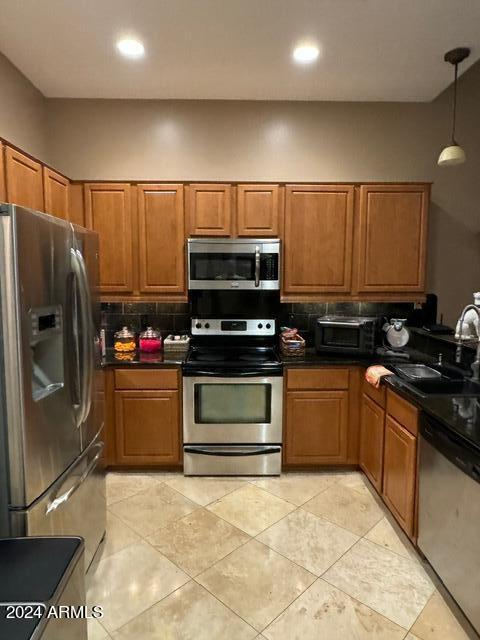 kitchen with decorative light fixtures, appliances with stainless steel finishes, tasteful backsplash, sink, and light tile floors