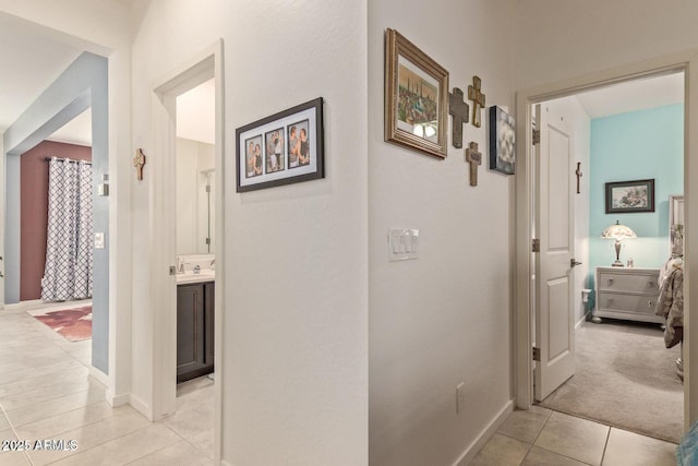 hallway with a sink, baseboards, and light tile patterned floors