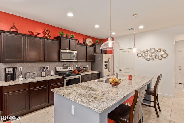 kitchen featuring a center island with sink, appliances with stainless steel finishes, a sink, a kitchen bar, and backsplash