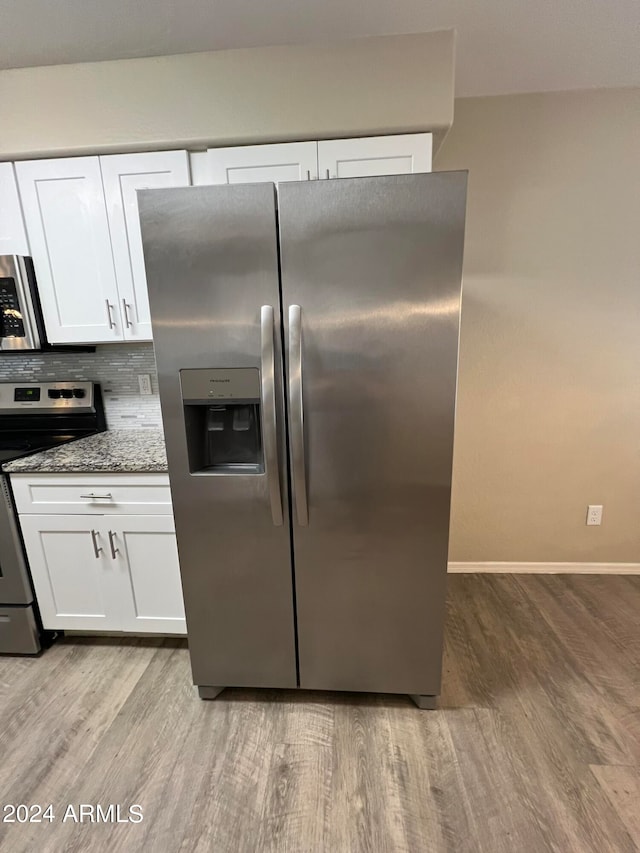 kitchen with light hardwood / wood-style floors, white cabinets, appliances with stainless steel finishes, and stone countertops