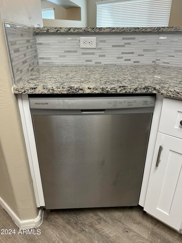 interior details featuring tasteful backsplash, light stone counters, dishwasher, hardwood / wood-style flooring, and white cabinetry