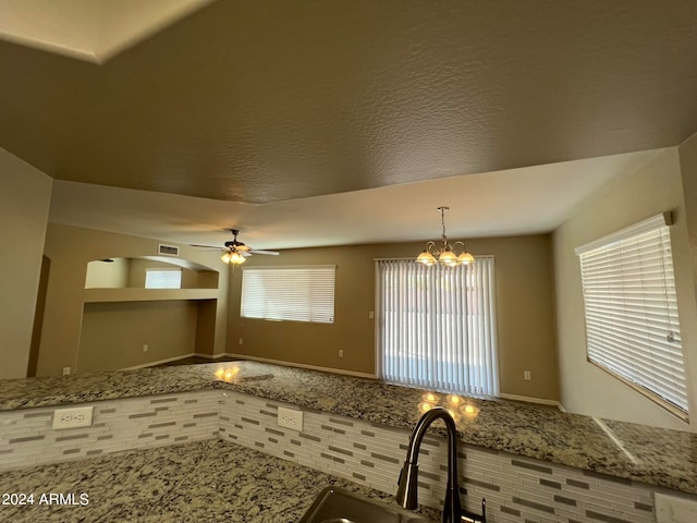 kitchen with light stone countertops, ceiling fan with notable chandelier, decorative light fixtures, and sink