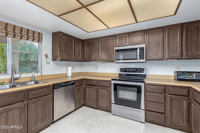 kitchen with light countertops, dark brown cabinets, appliances with stainless steel finishes, and a sink