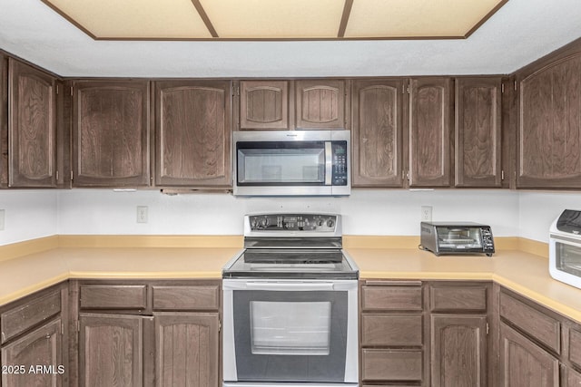 kitchen with stainless steel appliances, a toaster, dark brown cabinets, and light countertops