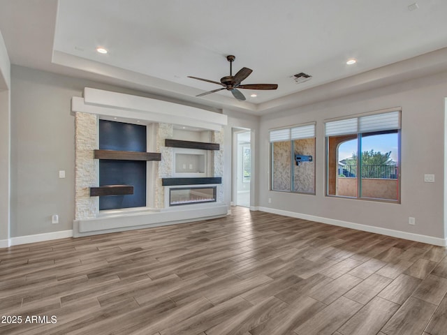 16881 W Merrell St, Goodyear, AZ 85395 - unfurnished living room with a large fireplace, a tray ceiling, wood finished floors, baseboards, and ceiling fan