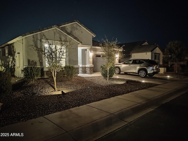 view of front of house with driveway, stone siding, a garage, and stucco siding