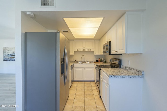 kitchen featuring sink, white cabinetry, light stone counters, light tile patterned floors, and appliances with stainless steel finishes