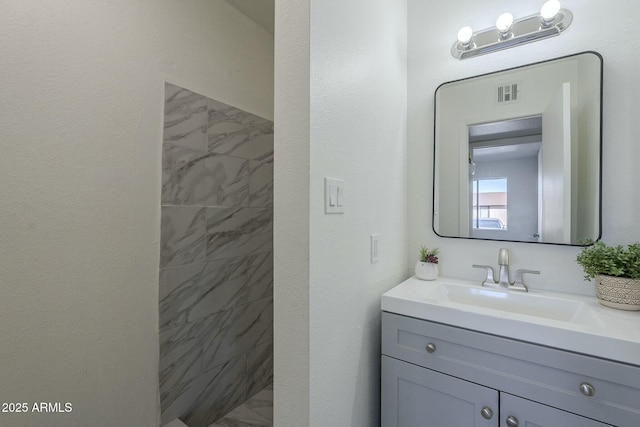 bathroom featuring tiled shower and vanity