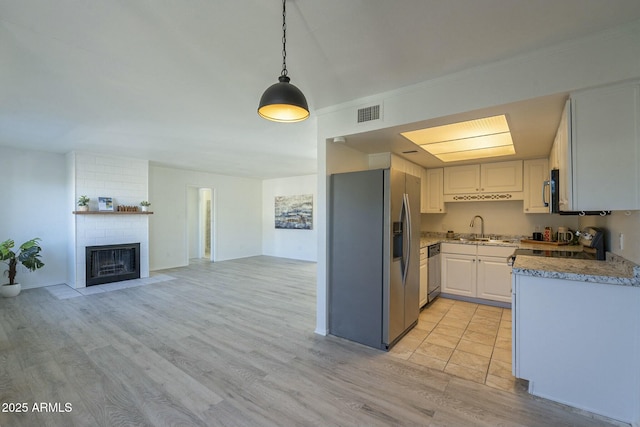 kitchen featuring a fireplace, sink, white cabinets, hanging light fixtures, and stainless steel appliances