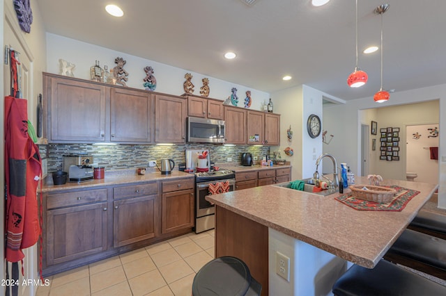 kitchen with appliances with stainless steel finishes, a breakfast bar, sink, a center island with sink, and decorative light fixtures