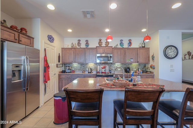 kitchen with a kitchen island with sink, decorative backsplash, light tile patterned floors, decorative light fixtures, and stainless steel appliances