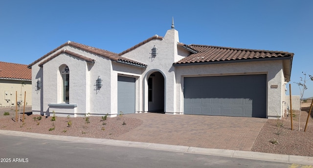 mediterranean / spanish home featuring stucco siding, decorative driveway, an attached garage, a chimney, and a tiled roof