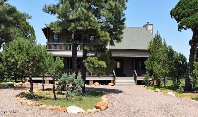 view of front of home with a balcony, a porch, a shingled roof, and a chimney