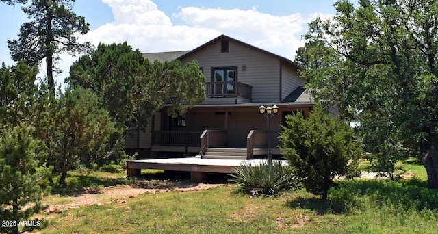 rear view of house with a balcony, a lawn, and roof with shingles