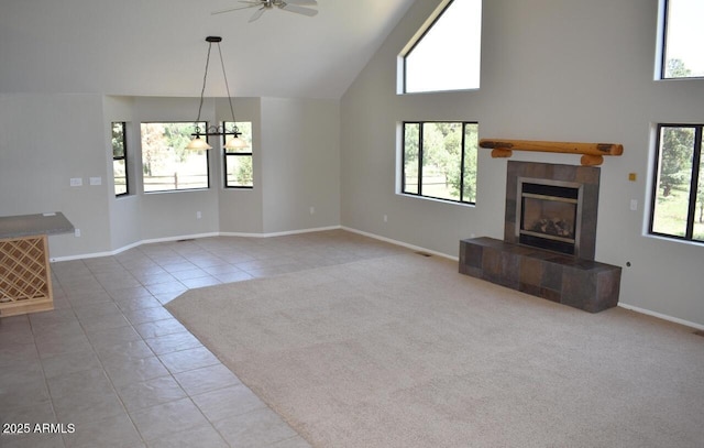 unfurnished living room with a tiled fireplace, light tile patterned flooring, ceiling fan with notable chandelier, and a healthy amount of sunlight