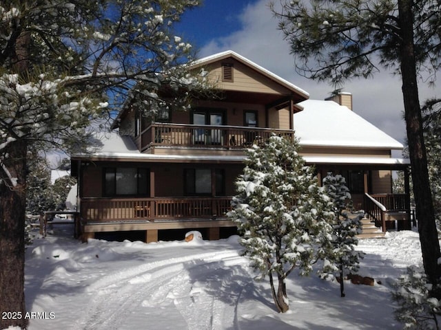 snow covered back of property with a balcony and a chimney