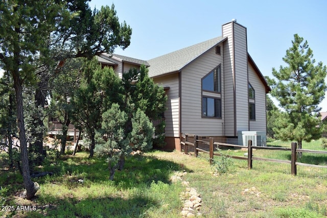 view of home's exterior featuring cooling unit, a shingled roof, fence, and a chimney