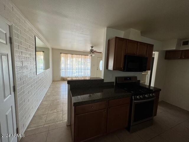 kitchen featuring gas range, ceiling fan, light tile patterned floors, kitchen peninsula, and brick wall