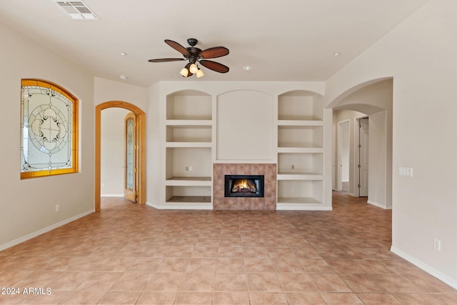 unfurnished living room featuring ceiling fan, built in shelves, light tile patterned floors, and a tile fireplace