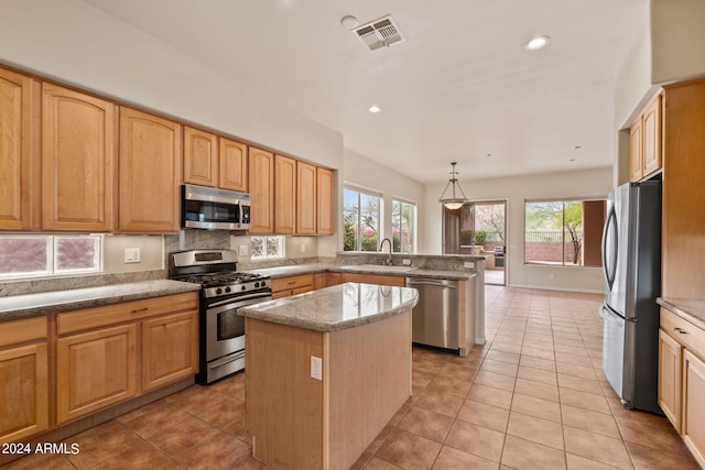 kitchen with pendant lighting, a kitchen island, sink, stainless steel appliances, and light tile patterned floors