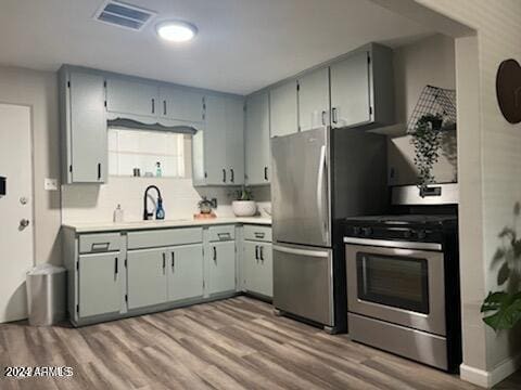 kitchen with gray cabinetry, stainless steel appliances, sink, and light wood-type flooring