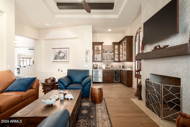 living room with a tray ceiling, a tile fireplace, bar, wine cooler, and light hardwood / wood-style flooring