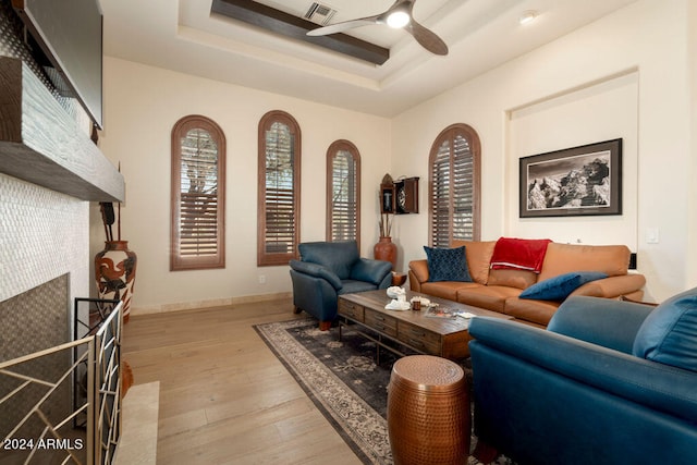 living room featuring ceiling fan, light wood-type flooring, and a raised ceiling