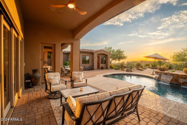 pool at dusk featuring an outdoor hangout area, pool water feature, a patio area, and ceiling fan