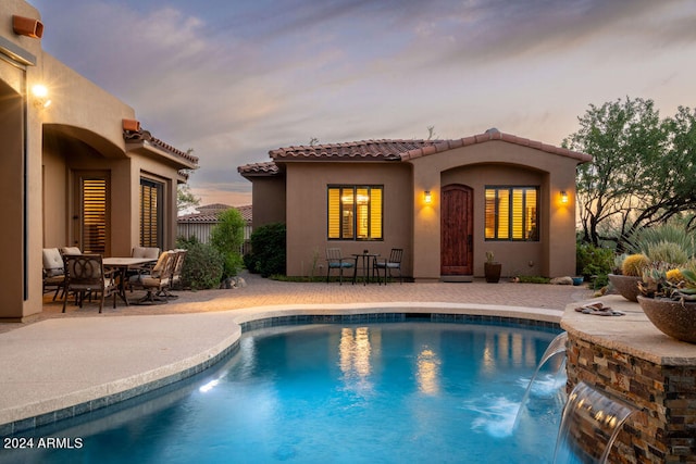 pool at dusk with a patio area and pool water feature