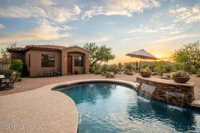 pool at dusk featuring a patio and pool water feature