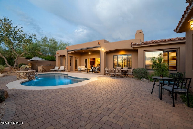 pool at dusk with pool water feature and a patio