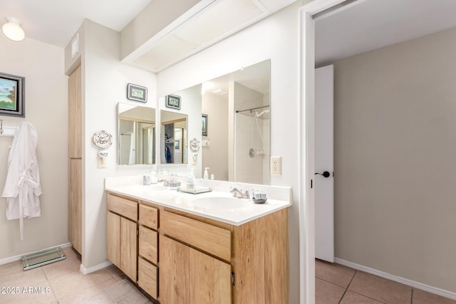 full bath with baseboards, double vanity, a sink, tile patterned flooring, and a shower