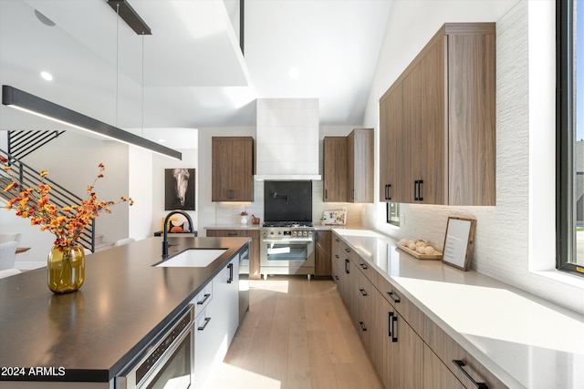 kitchen with sink, light hardwood / wood-style flooring, decorative backsplash, high end range, and custom range hood