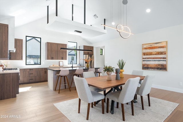 dining space with sink, high vaulted ceiling, light hardwood / wood-style floors, and an inviting chandelier